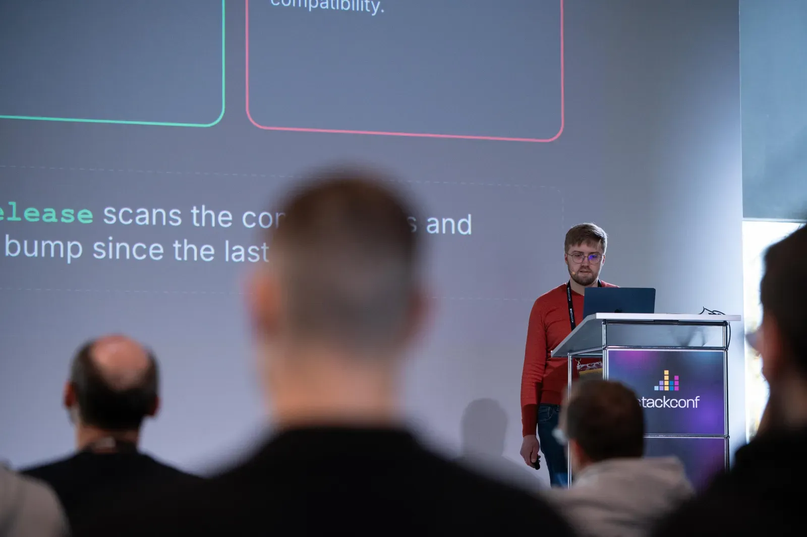 Daniel Schock am Rednerpult der stackconf 2026, davor das Publikum im abgedunkelten Saal